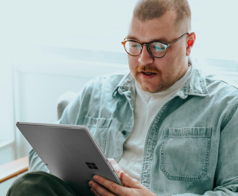 man in denim jacket and glasses sitting working on a tablet