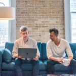 two men working on a laptop on a blue sofa