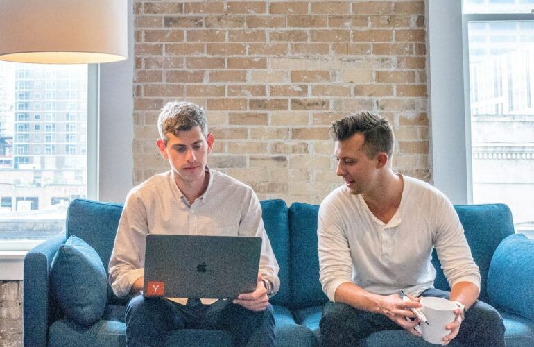 two men working on a laptop on a blue sofa
