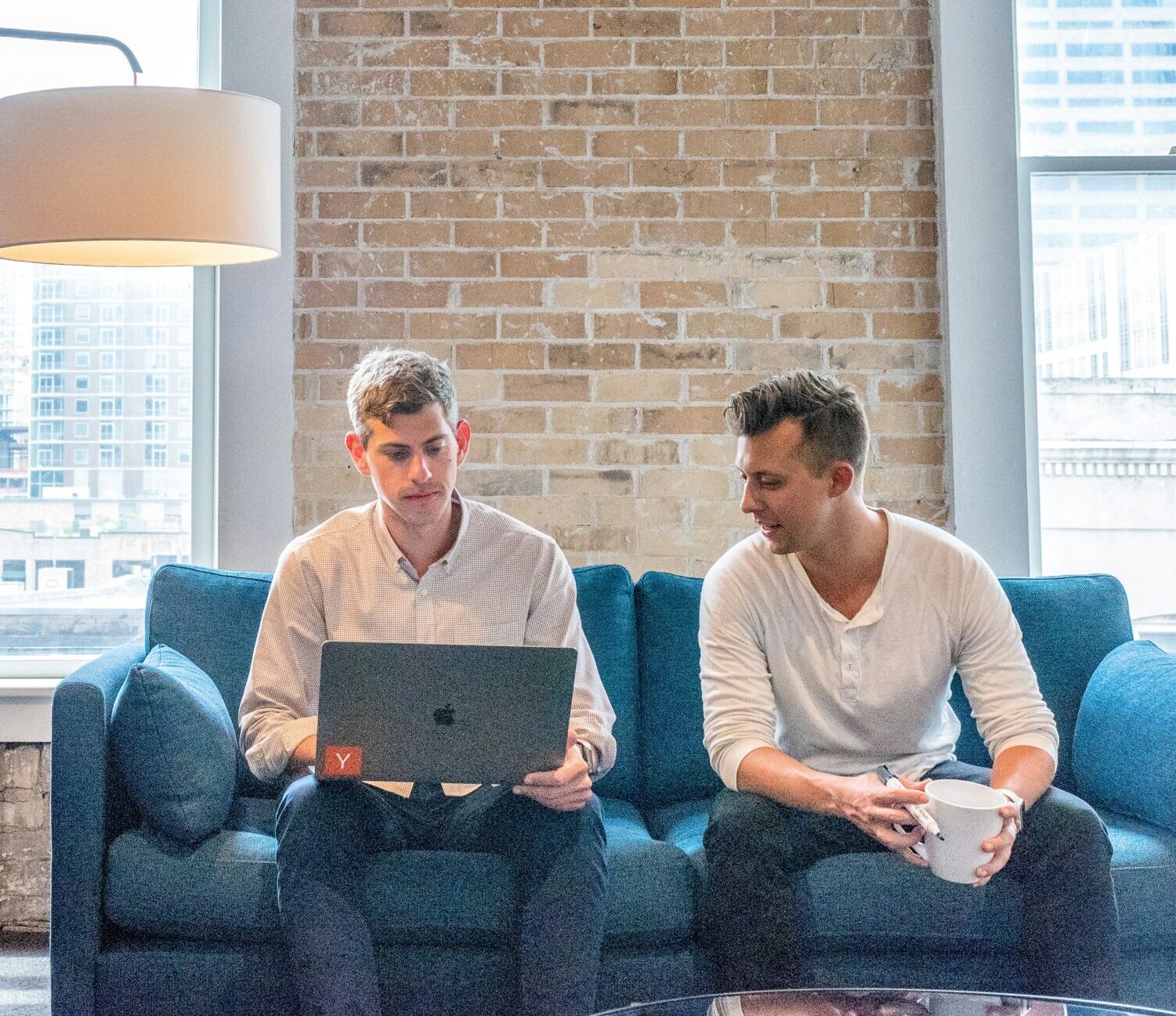 two men working on a laptop on a blue sofa