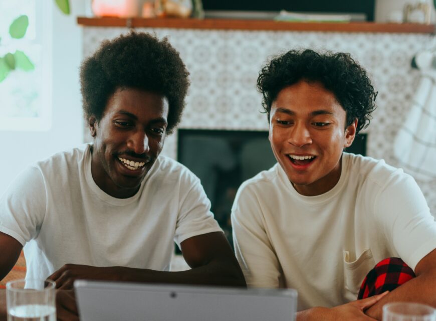 two men smiling using their laptop at a desk