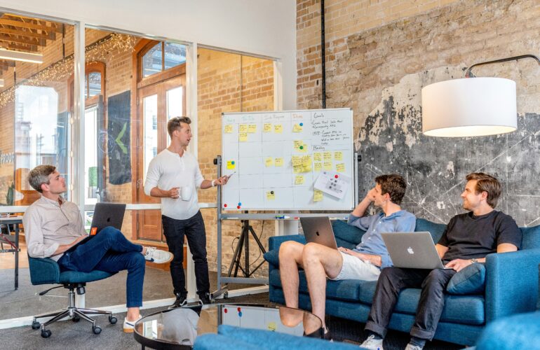 A group of men with laptops talking around a white board in an office
