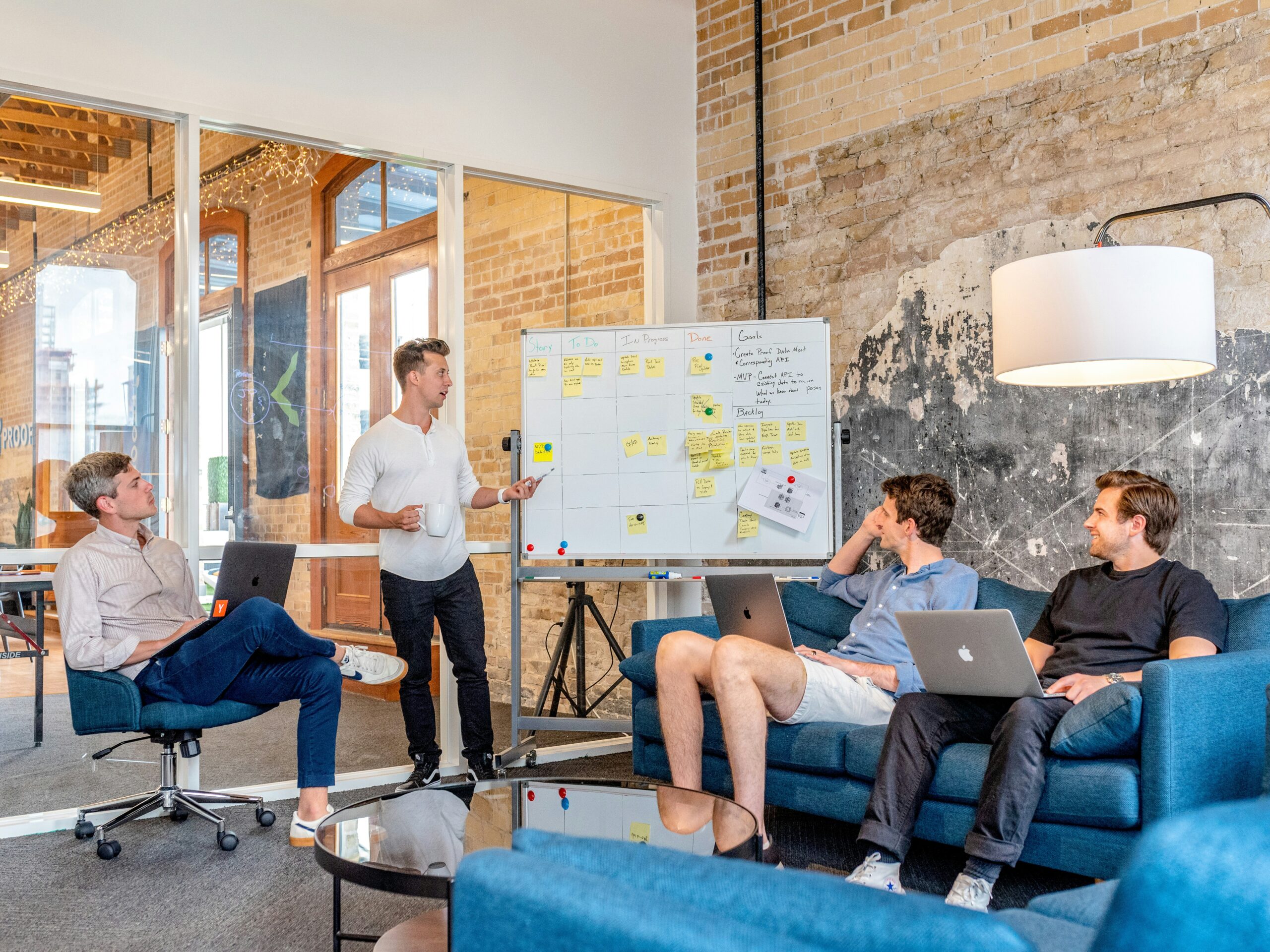 A group of men with laptops talking around a white board in an office
