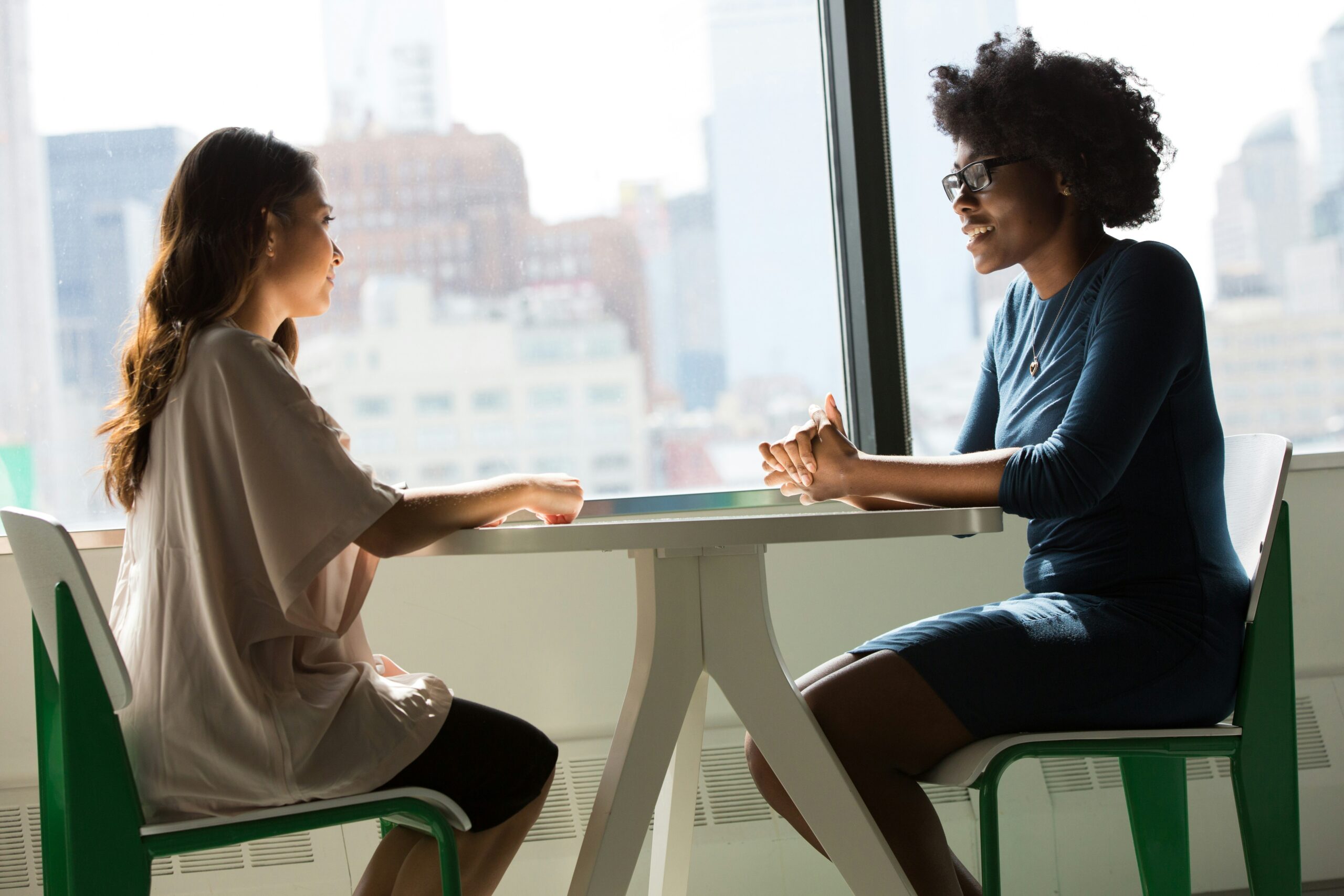 two women sitting at a small table in an office having a business conversation