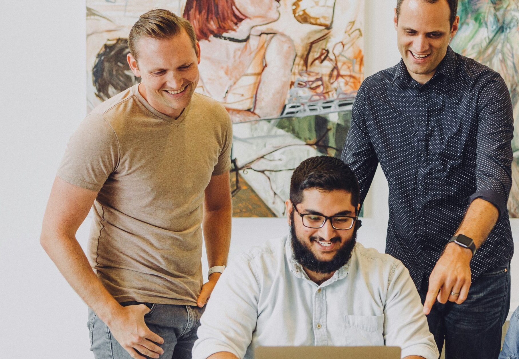 four people in an office looking at a Mac laptop