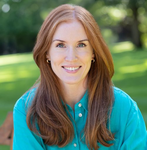 red-hair-woman-green-shirt-smile red haired lady in a green shirt sitting on a garden bench smiling