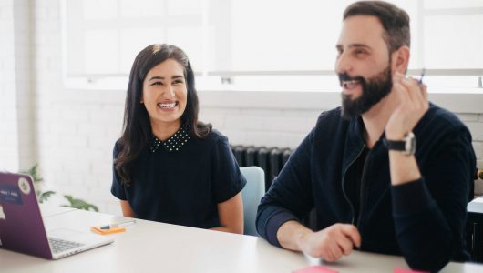 a man and woman in an office wearing black smiling at a work table