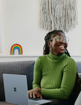 woman-sitting-sofa-laptop woman in green jumper sitting on a sofa with a laptop smiling